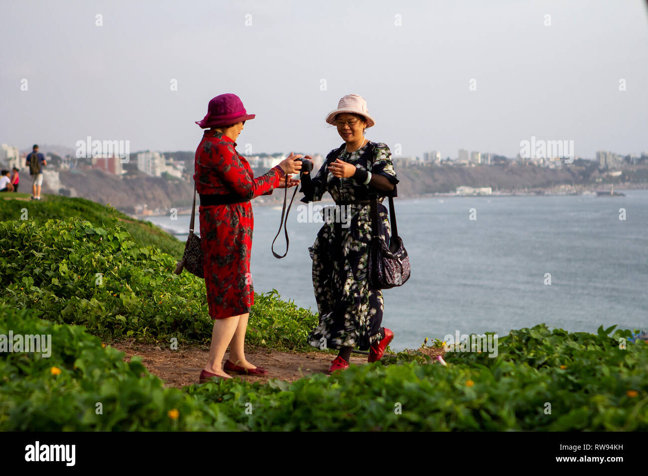 Lima, Peru - February 22 2019: Asian tourists taking photos of the sunset at Malecón de la Costa Verde, woman passing the camera to a friend Stock Photo