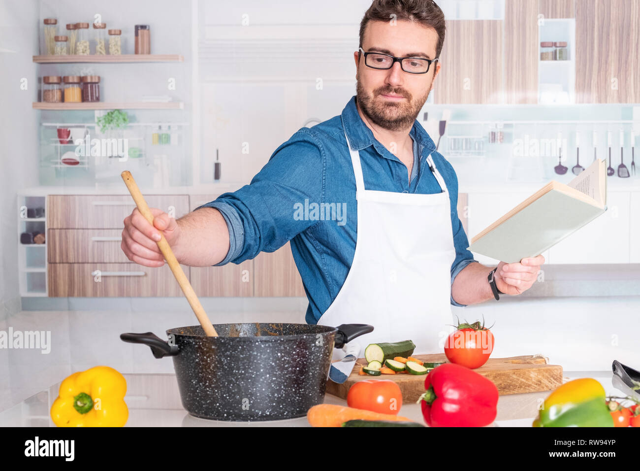 Man cooking at home reading from recipe book Stock Photo Alamy