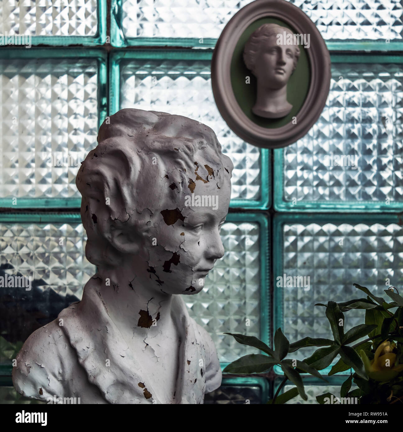 Chipped white head sculpture against glass block wall with antique