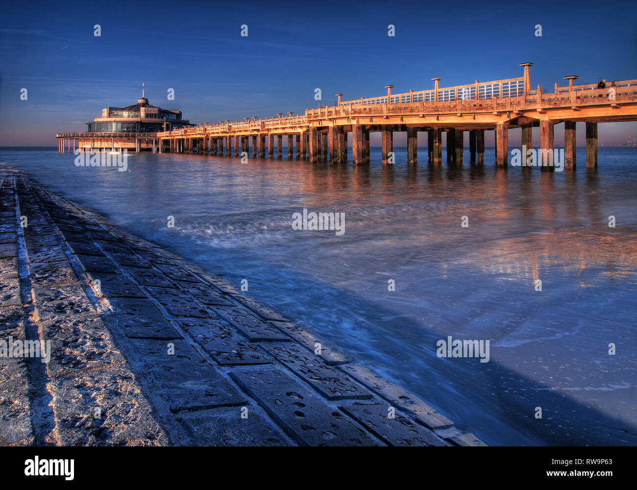 An artistic long exposure of the pier in Blankenberge with a view on the North Sea and a wave breaker, Belgium. Stock Photo