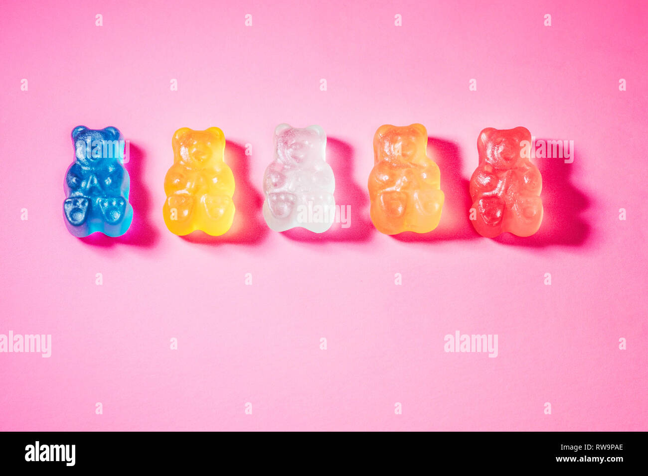 A close-up of five brightly-colored gummy bears, photographed on a pink background with poppy studio light. Stock Photo