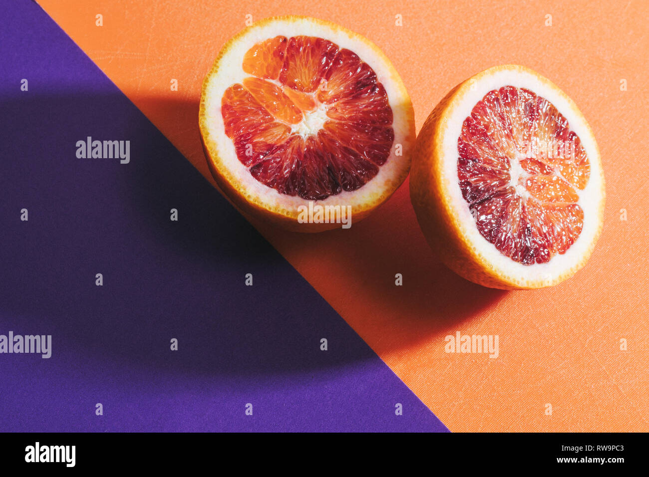 A graphic still life of a sliced blood orange on a colorful background, photographed with hard light and shadows in studio. Stock Photo