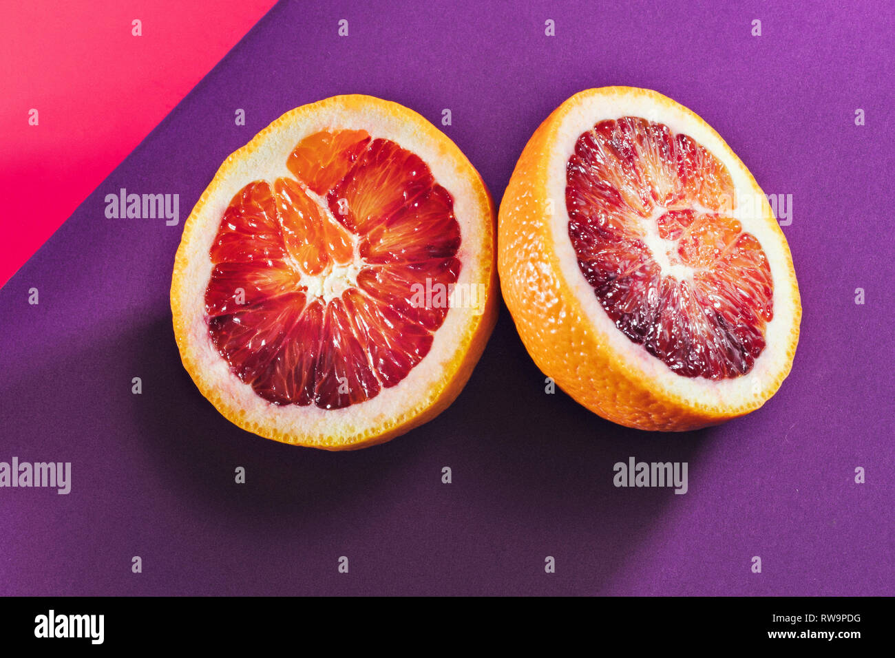 A graphic still life of a sliced blood orange on a colorful background, photographed with hard light and shadows in studio. Stock Photo