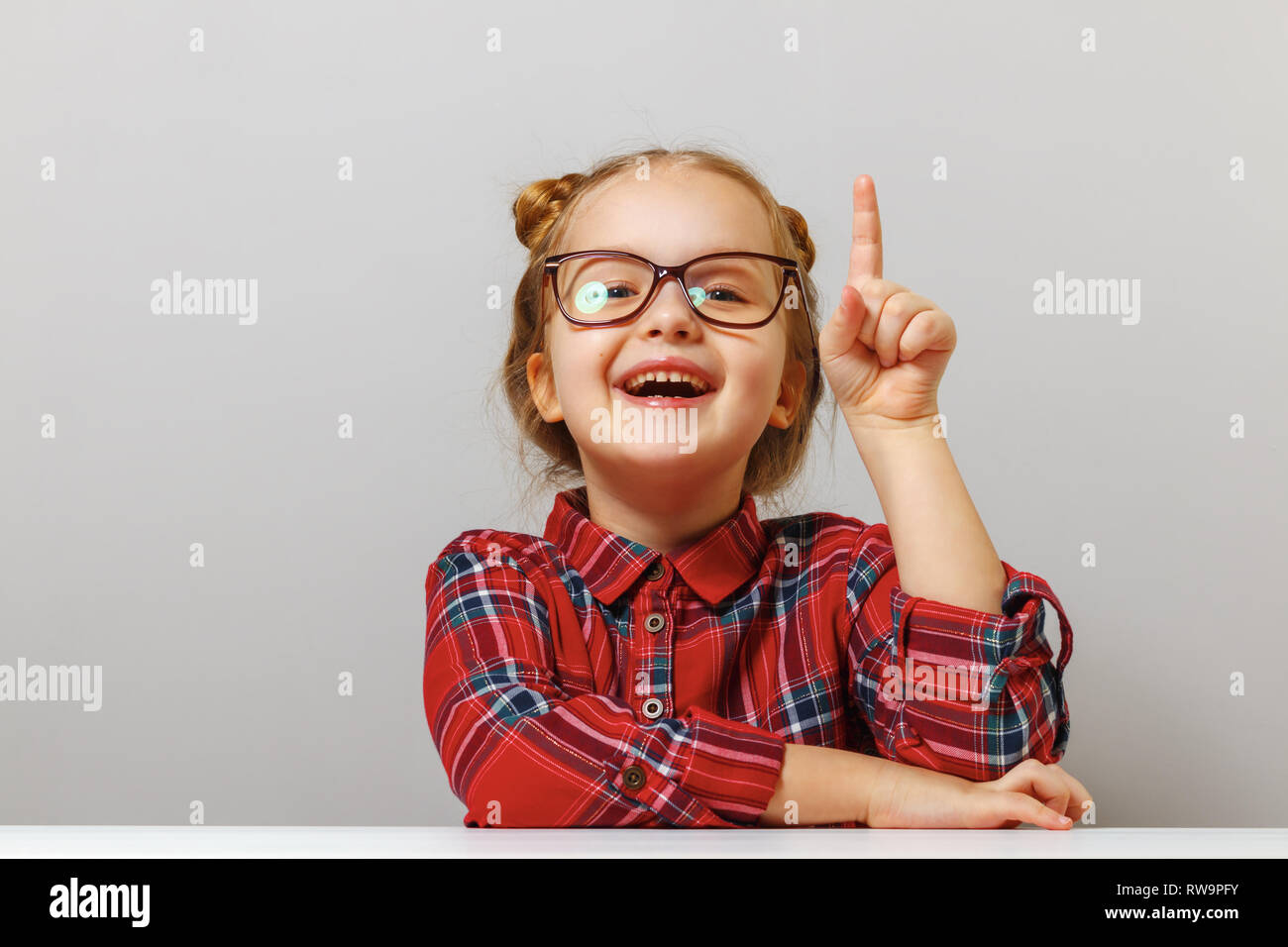 Back to school. Funny little girl with glasses points finger up. Education concept. Gray background Stock Photo