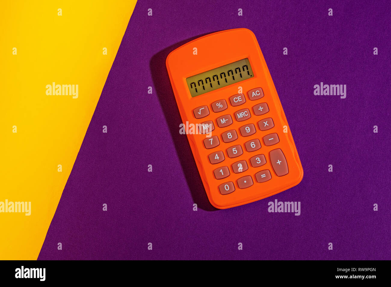 A graphic studio photo of an orange calculator on a purple and yellow background. Stock Photo