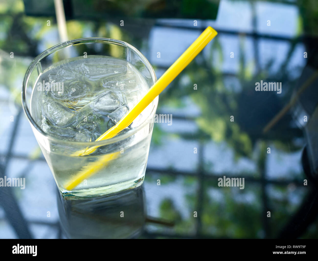 A glass of cold drinking water with ice and yellow straw on glass table ...