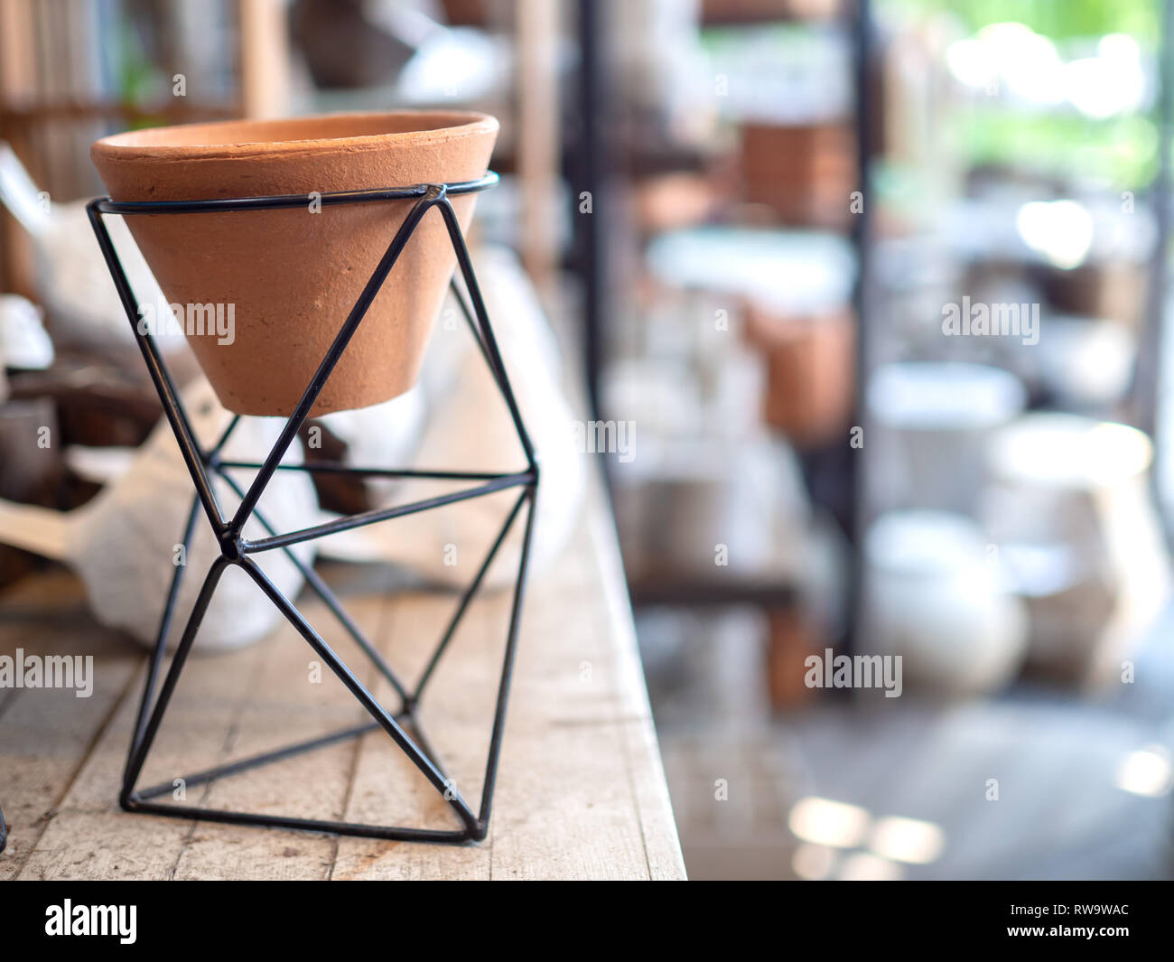 Empty small terracotta pot in modern black geometric Iron rack holder on wooden table with copy space. Stock Photo