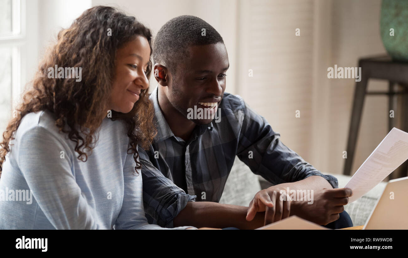 Happy mixed race couple check paper bills paying online Stock Photo