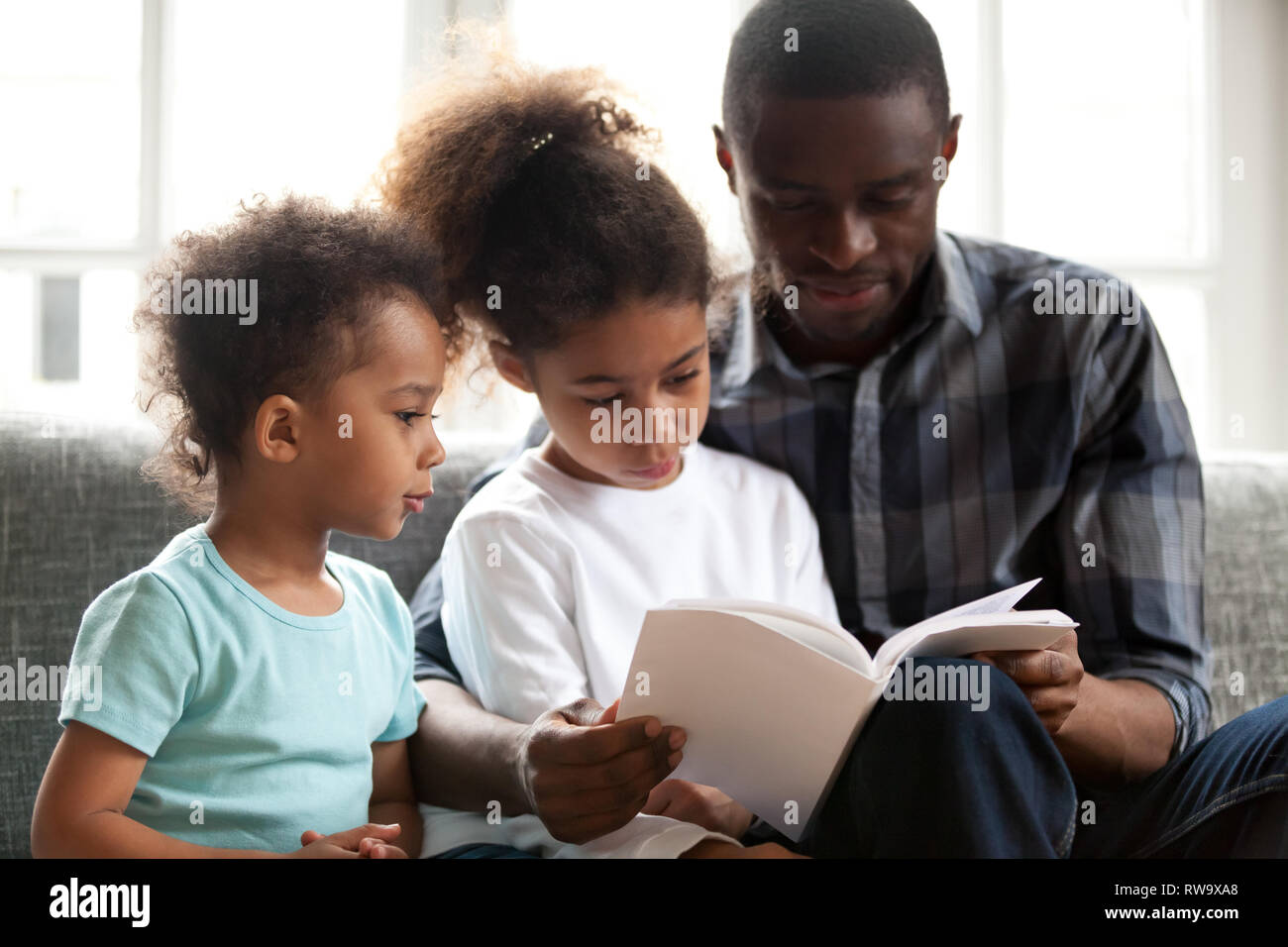 African American dad reading book to small kids Stock Photo