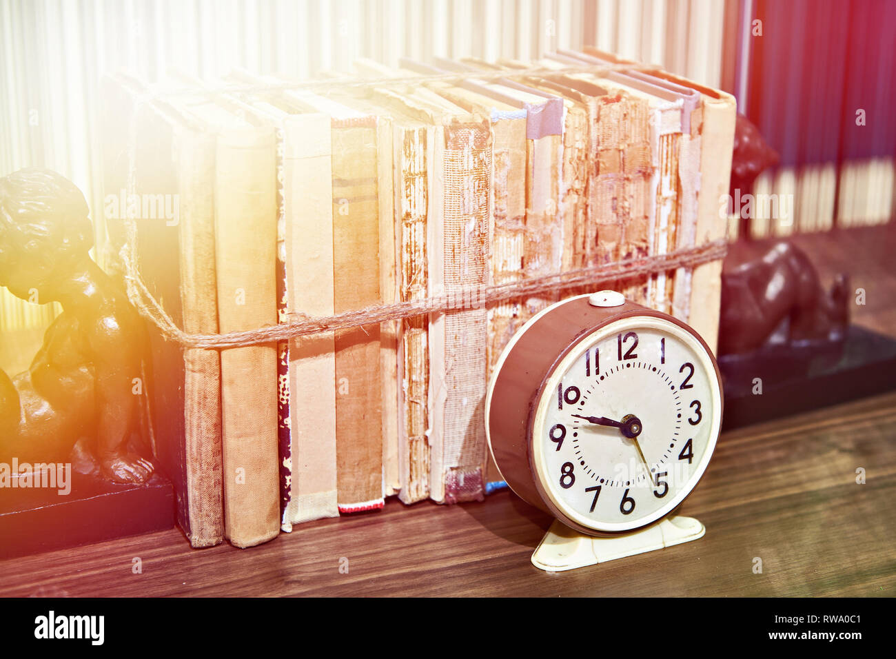Old books tied up with rope on shelf and alarm clock Stock Photo