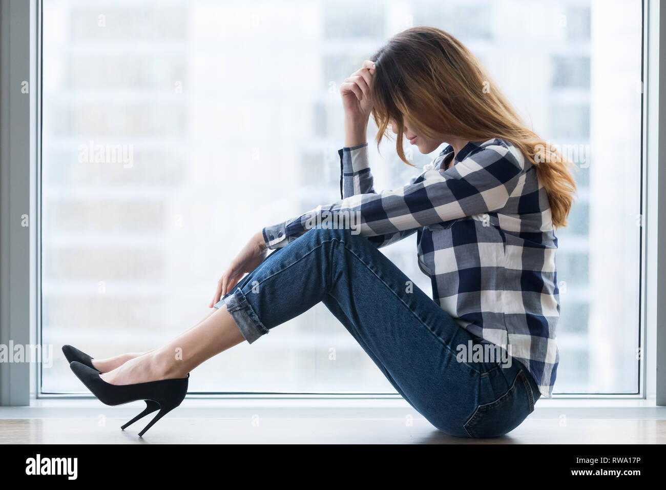 Depressed vulnerable young woman in trouble sitting on floor alone Stock Photo
