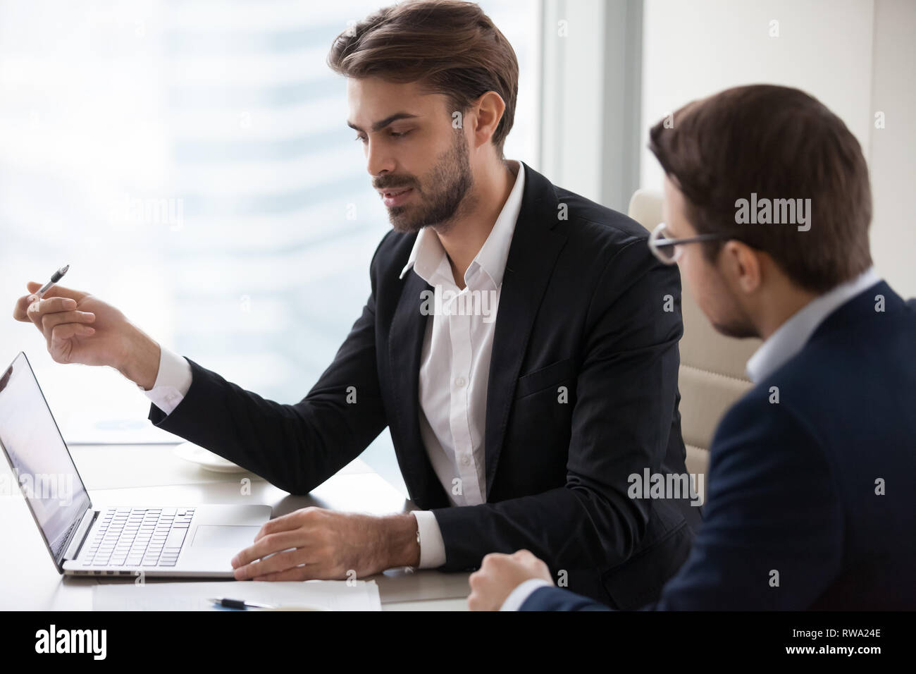 Serious businessman manager talking with client pointing at laptop Stock Photo