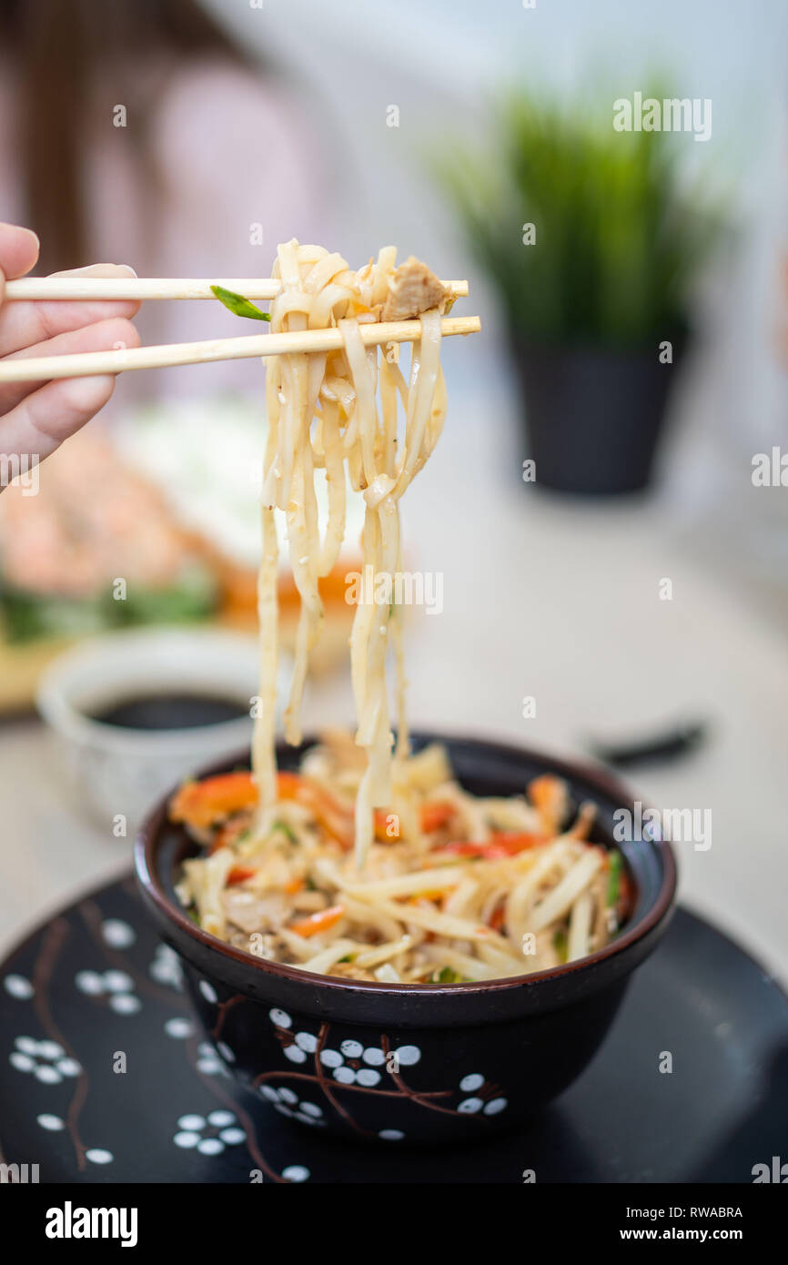 Close up of human hand grabbing noodles with chopsticks from a bowl with hot noodle soup. Stock Photo