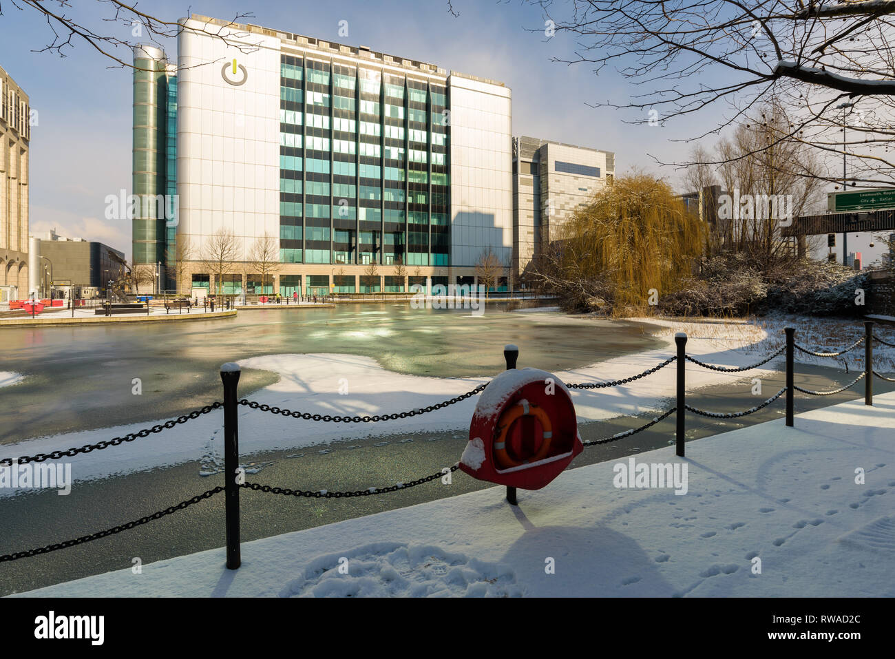 London, England - Feb 2018. Fresh snow covers the frozen pond next to East India DLR station in Poplar. In the background the Global Switch building. Stock Photo
