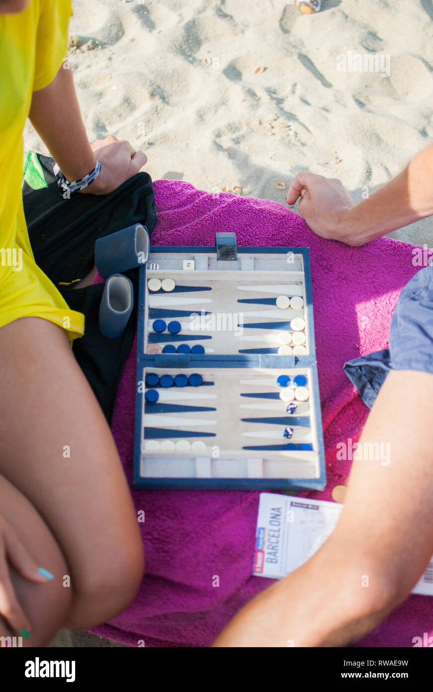 Two people playing board game on pink towel on sand at