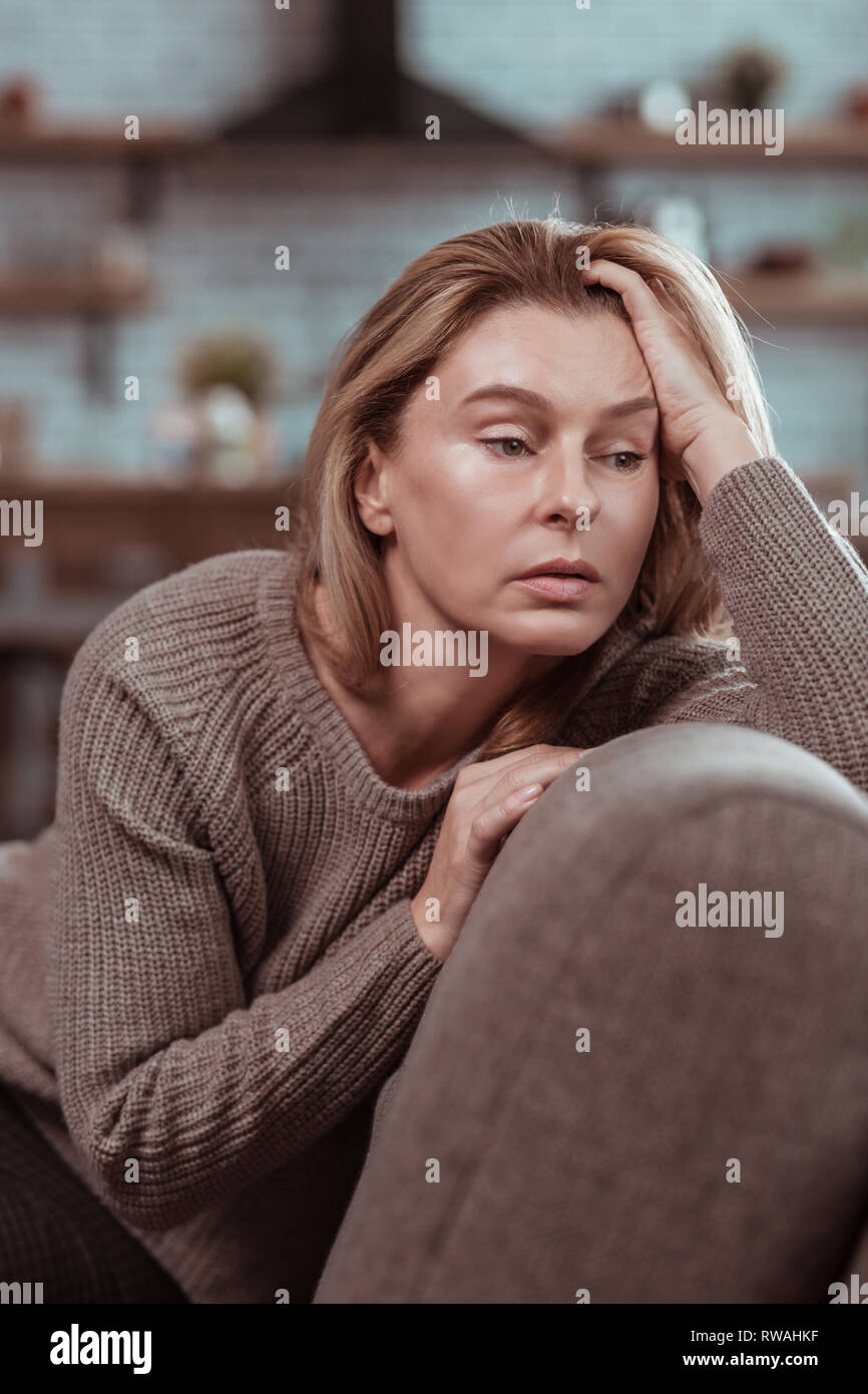 Dark-eyed woman sitting on sofa and feeling in despair Stock Photo