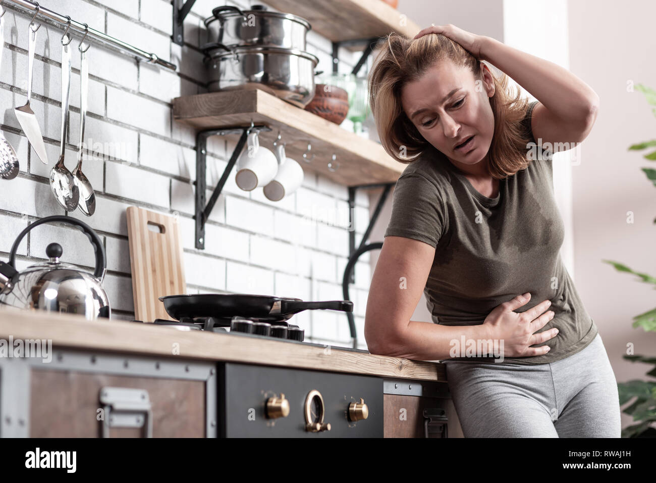 Woman standing near cooker in kitchen suffering from pain Stock Photo