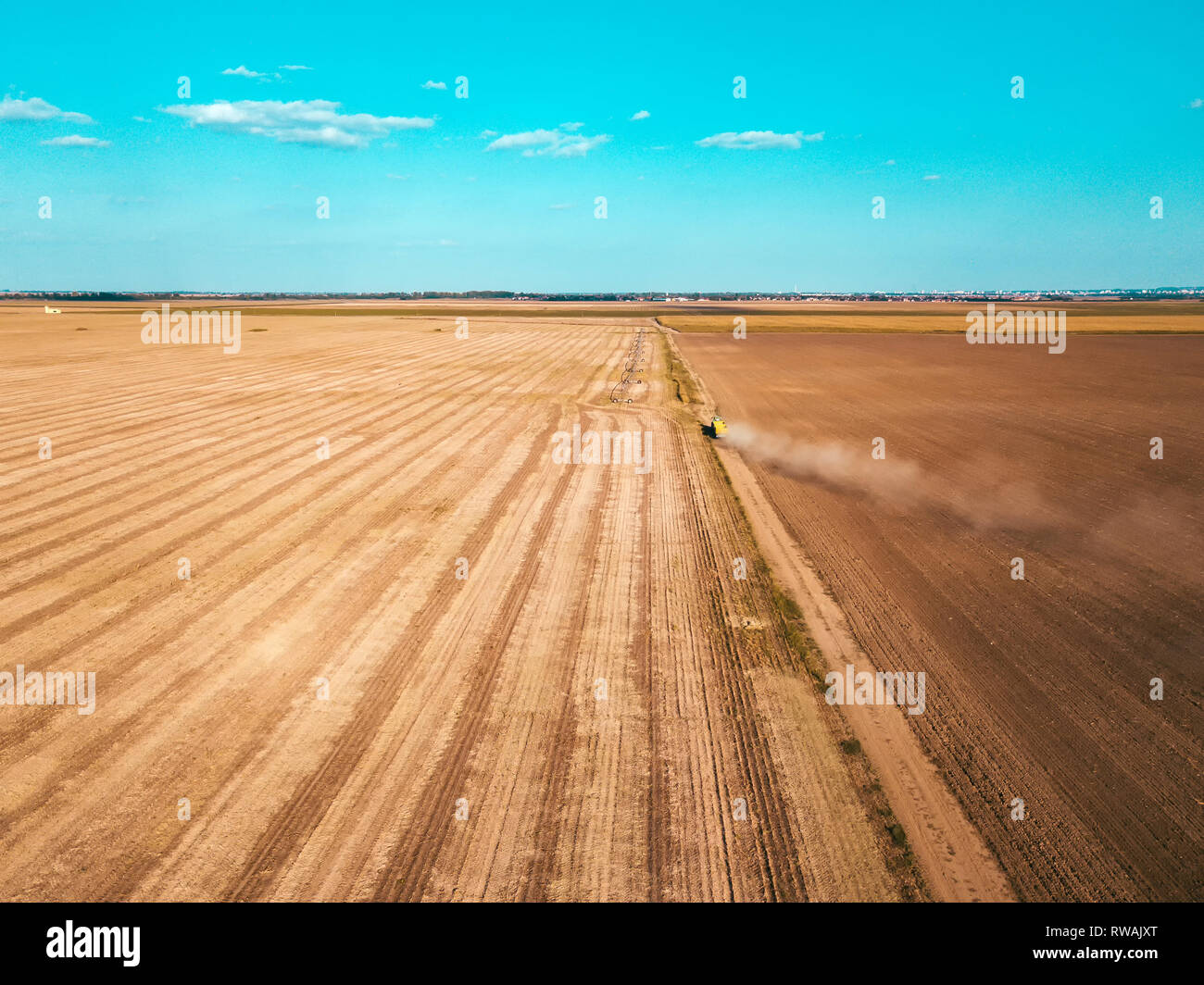 Aerial view of agricultural tractor on dirt road surrounded by ploughed and harvested fields Stock Photo