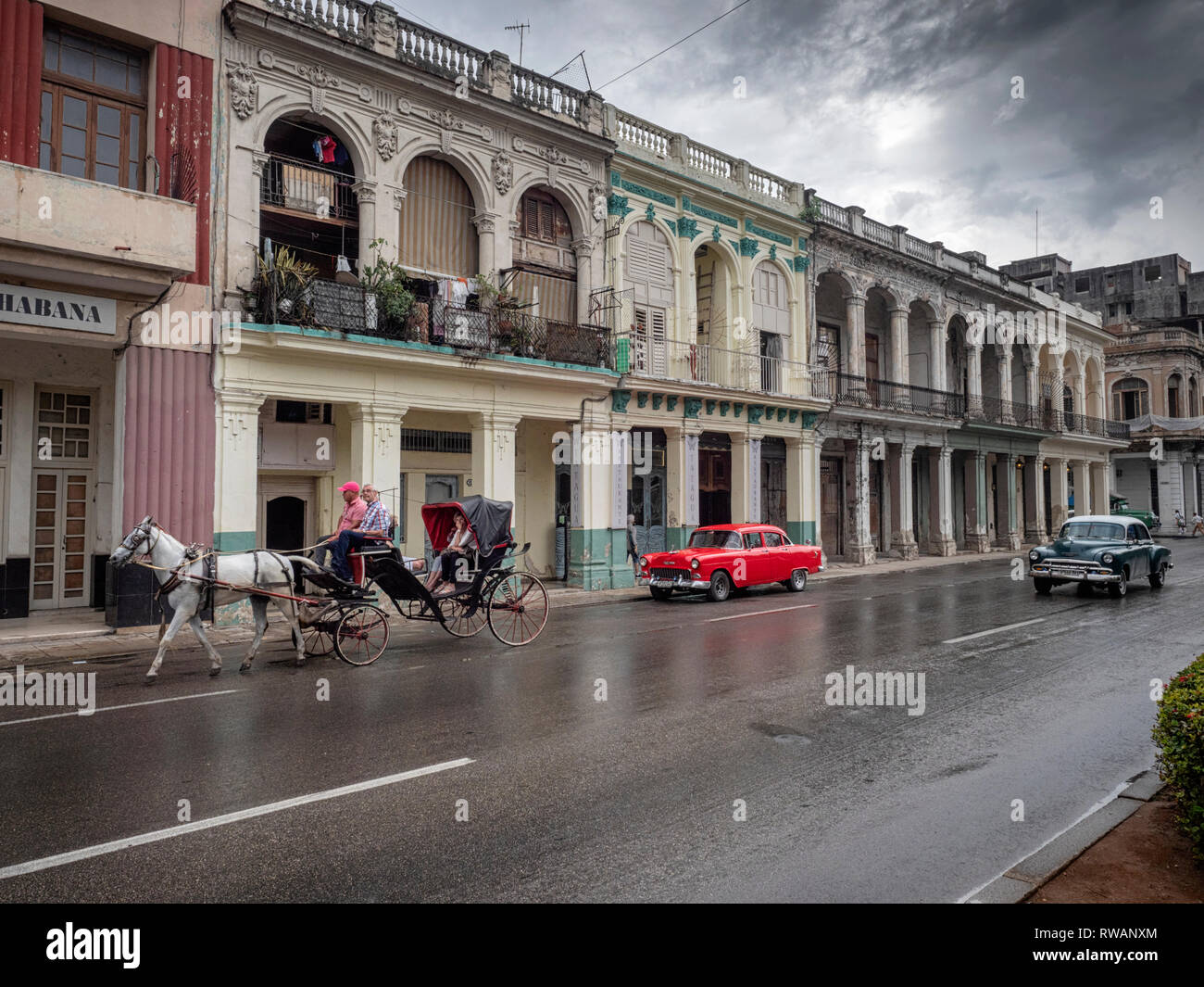 Old American cars and a horse and carriage on wet streets of Paseo de Marti after a rain storm in central Havana, Cuba Stock Photo