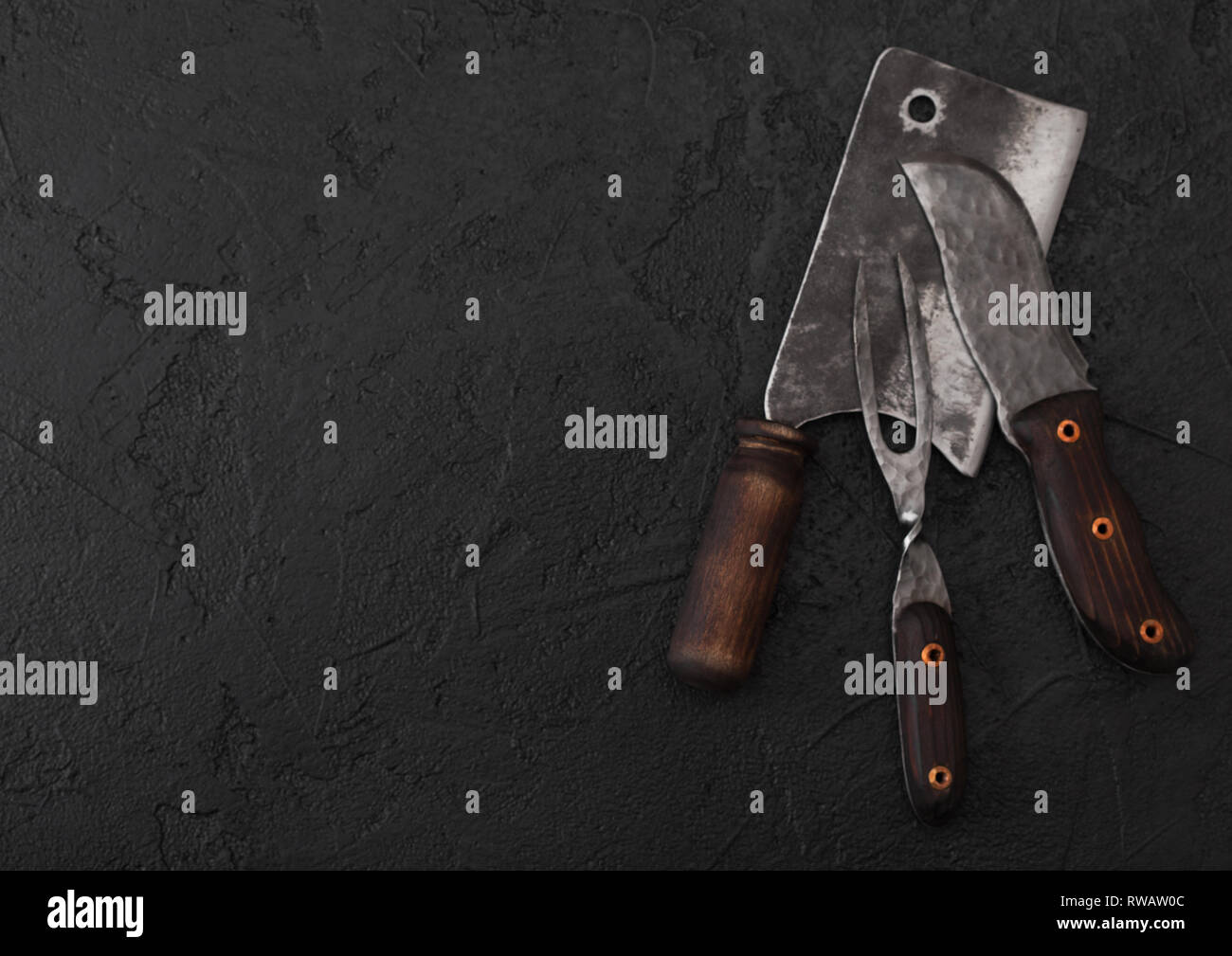 Vintage meat knife and fork and hatchet on black table background