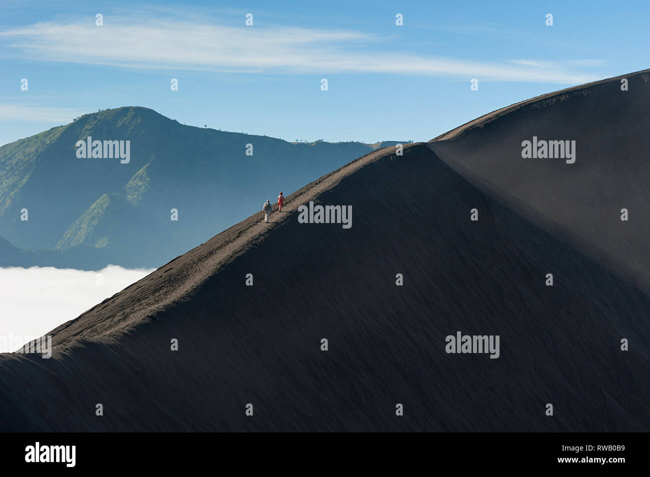 Beautiful morning mountain landscape with unrecognizable hikers on steep section of crater rim ridge. Stock Photo