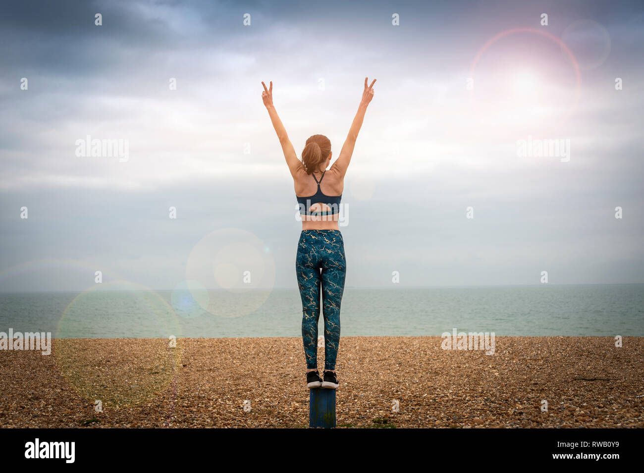 woman standing with arms raised on beach, back view, copyspace, lens flare Stock Photo