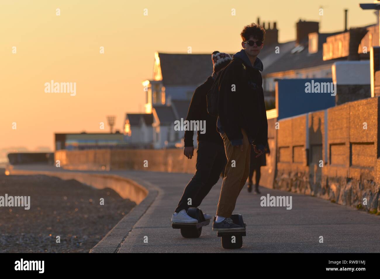 Sandgate, Kent/UK-February 15 2019: two 'onewheel' skateboard riders backlit by a setting sun on a seafront promenade Stock Photo