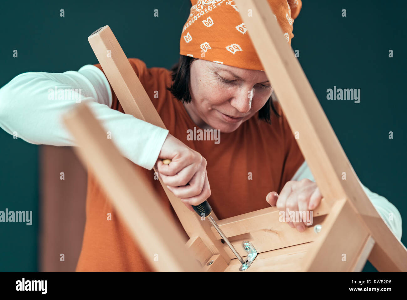 Female carpenter driving a screw into wooden chair in small business woodwork workshop, selective focus Stock Photo