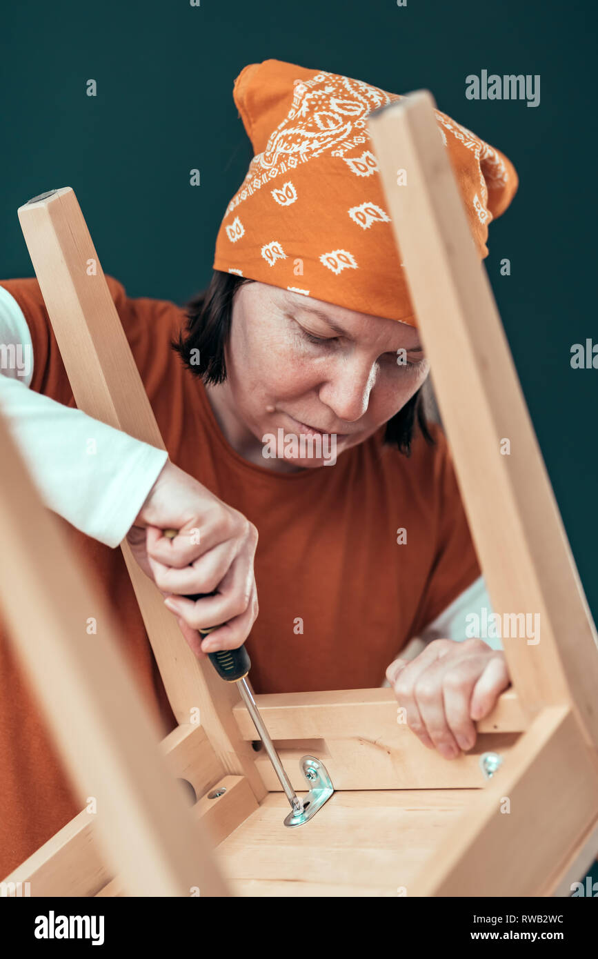 Female carpenter driving a screw into wooden chair in small business woodwork workshop, selective focus Stock Photo