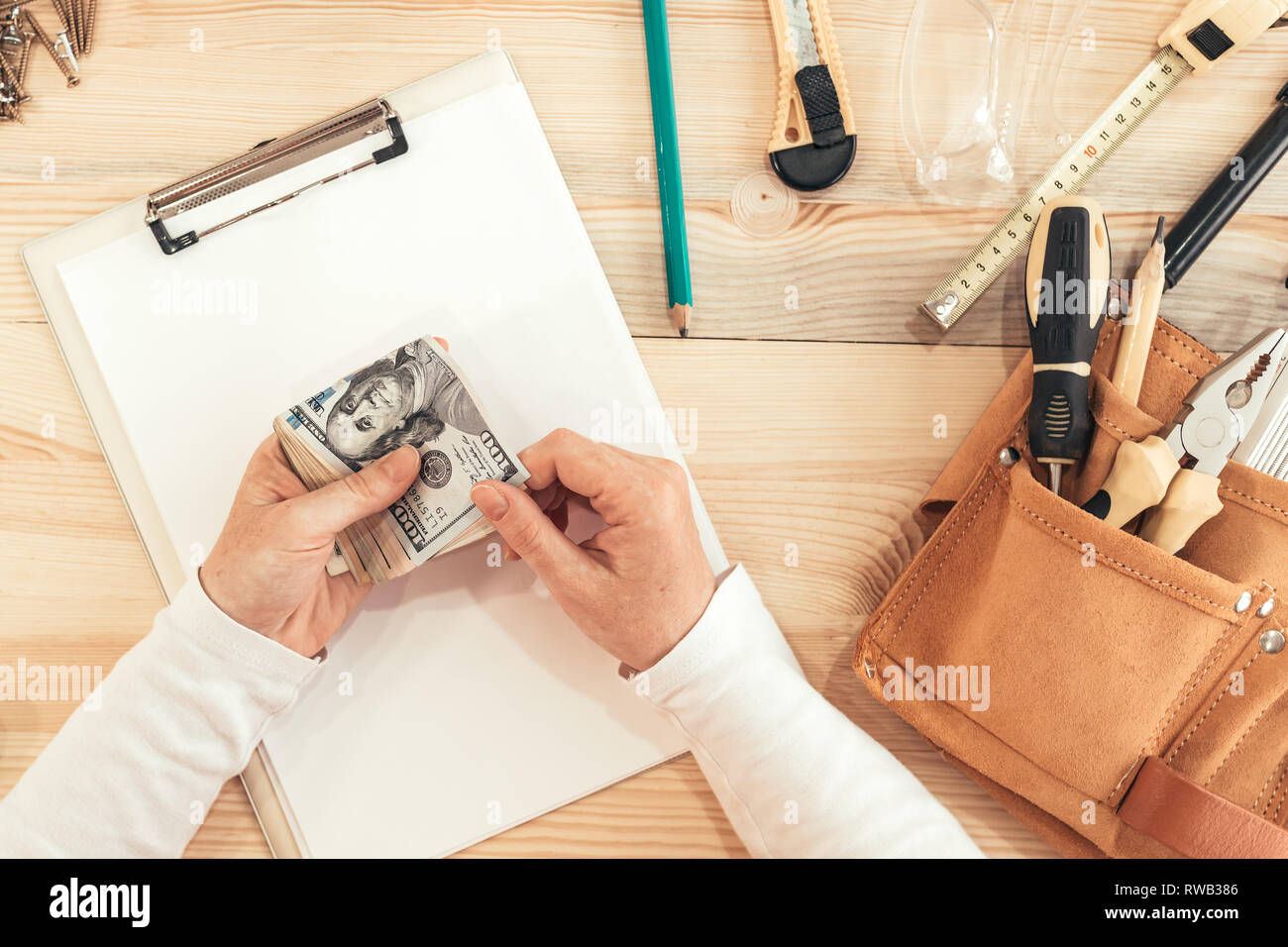 Female carpenter counting money, top view of hands holding US dollar paper currency Stock Photo