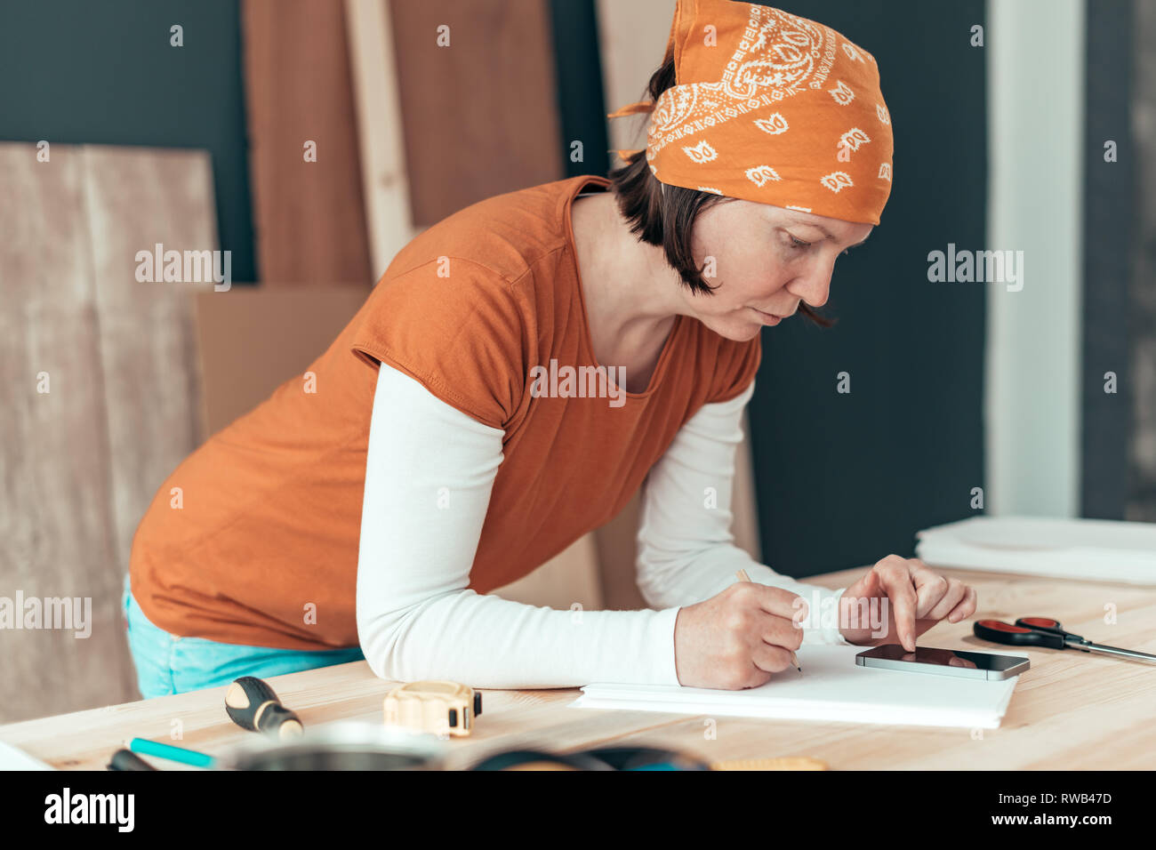 Female carpenter with head kerchief doing financial calculation in carpentry woodwork workshop Stock Photo