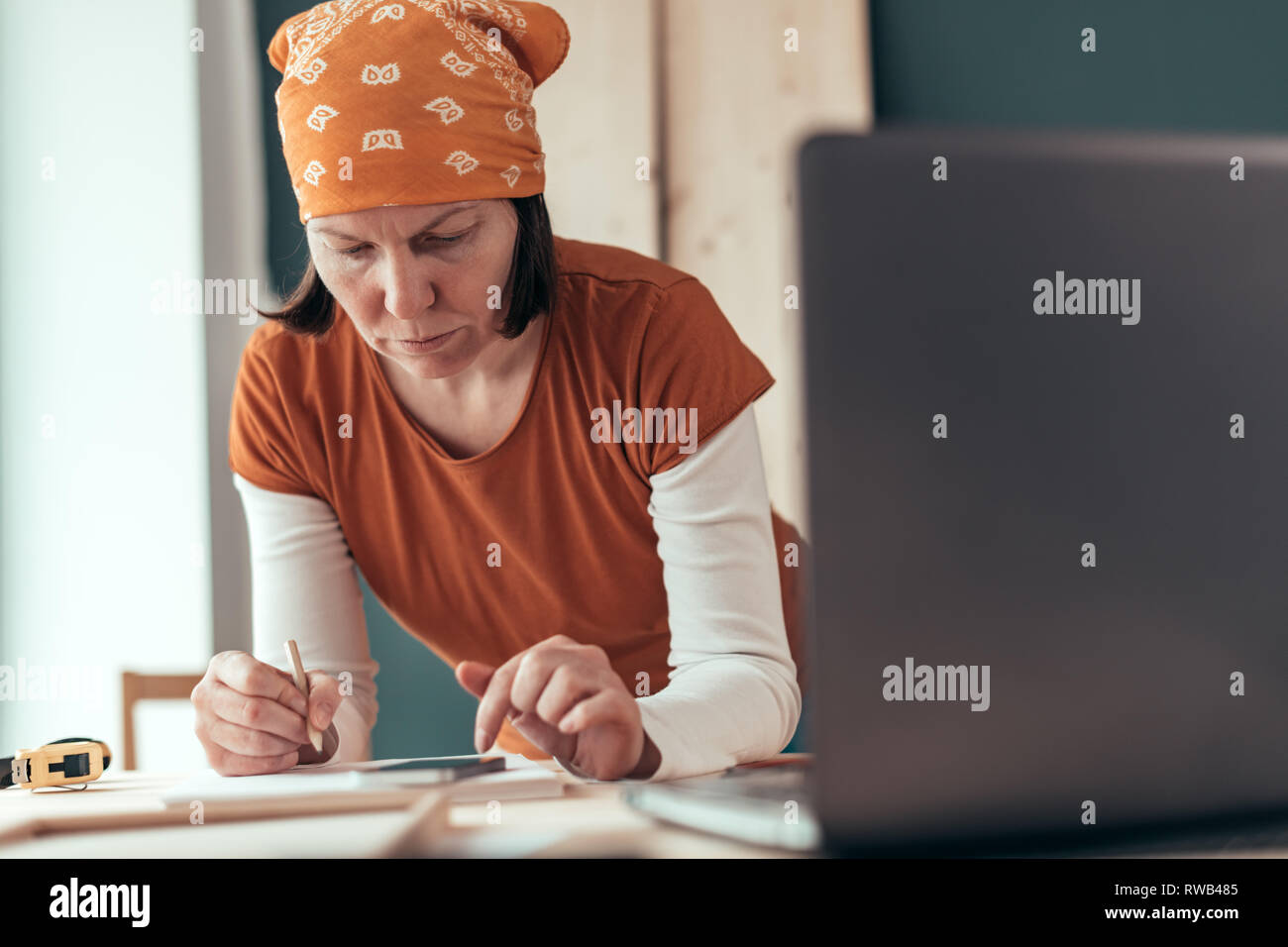 Female carpenter with head kerchief doing financial calculation in carpentry woodwork workshop Stock Photo