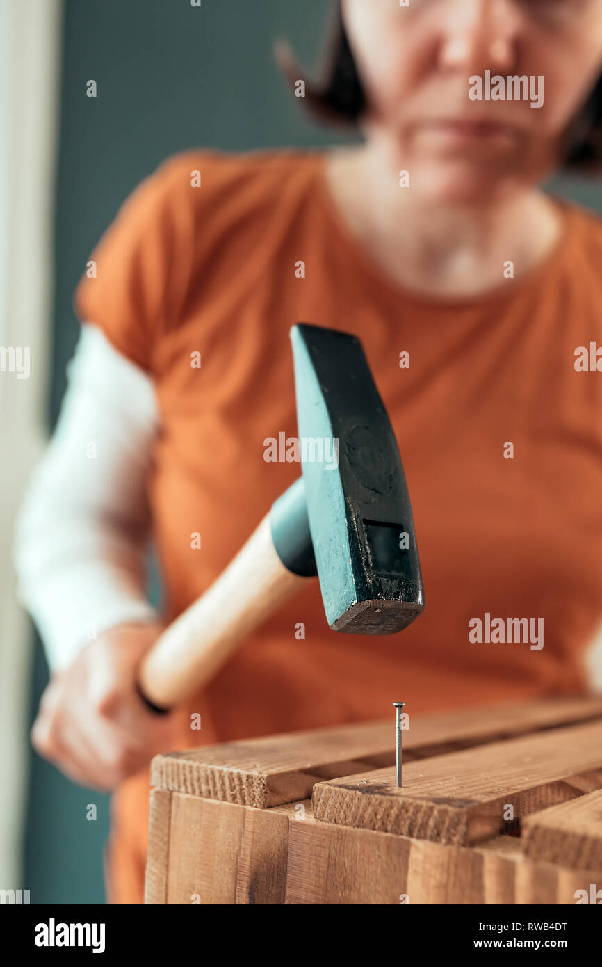 Female carpenter hammering nail into wooden crate in small business woodwork workshop, selective focus Stock Photo