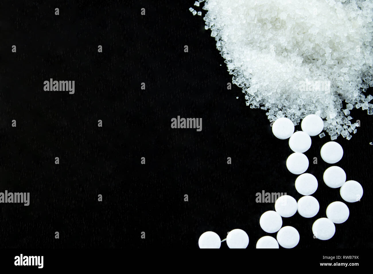 Sugar on a spoon and sweetener in pills on a black background. Stock Photo