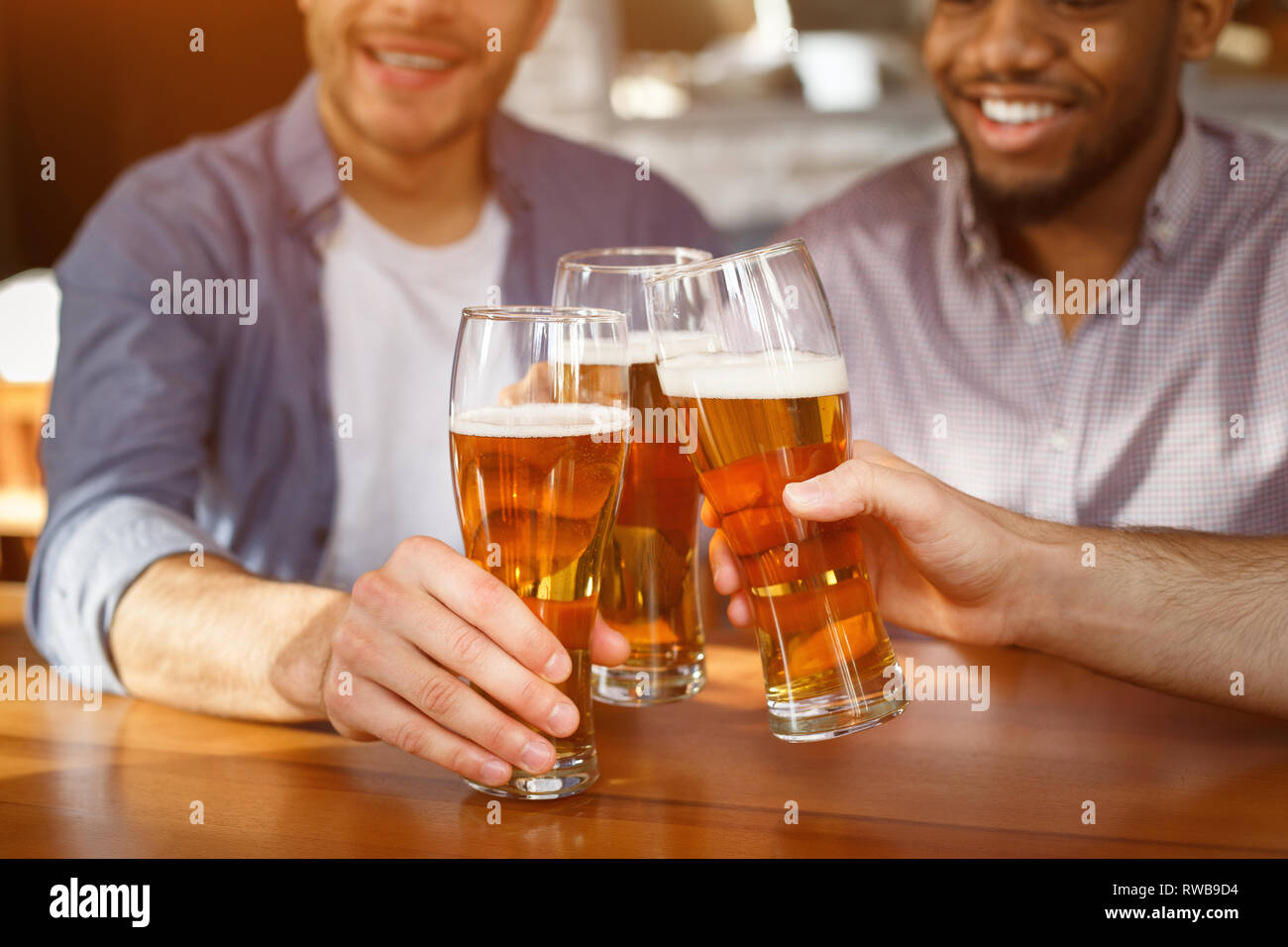 Best friends clinking beer glasses in bar, closeup Stock Photo