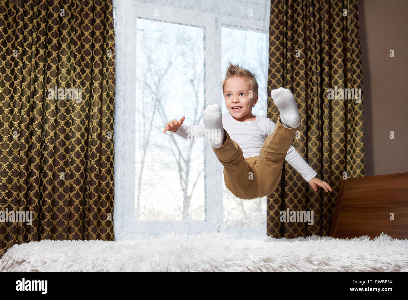 child fun home. Cheerful boy in motion jumping laughing on bed. Little kid of 6 years old happily plays morning in room. Stock Photo