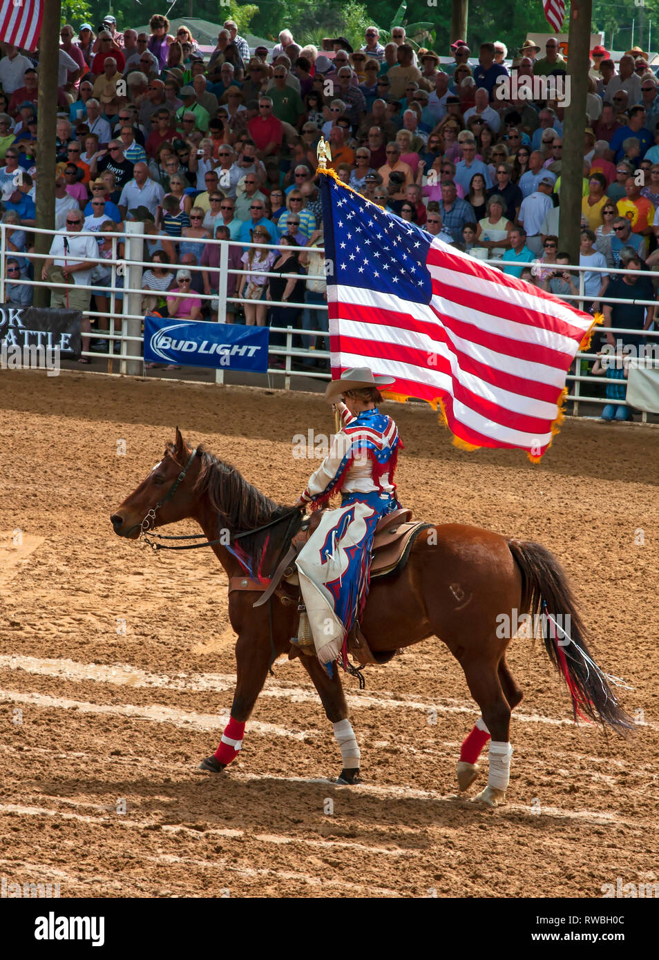 rodeo; cowgirl riding horse, carrying American flag; patriotic; western dress; red, white, blue, chaps; competition, crowd, spectators, Arcadia; FL; F Stock Photo