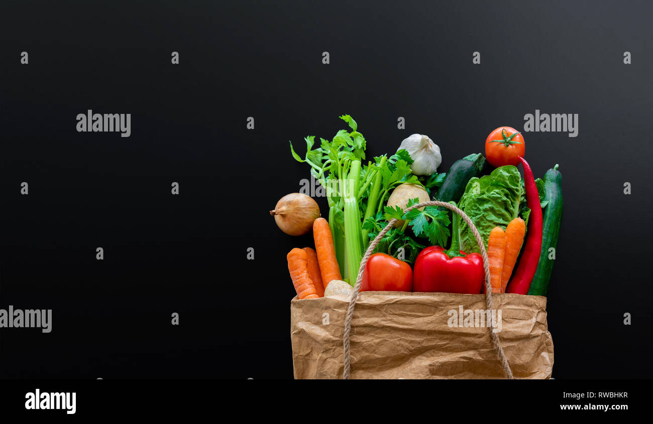 fresh organic vegetables in brown paper bag against dark table ...