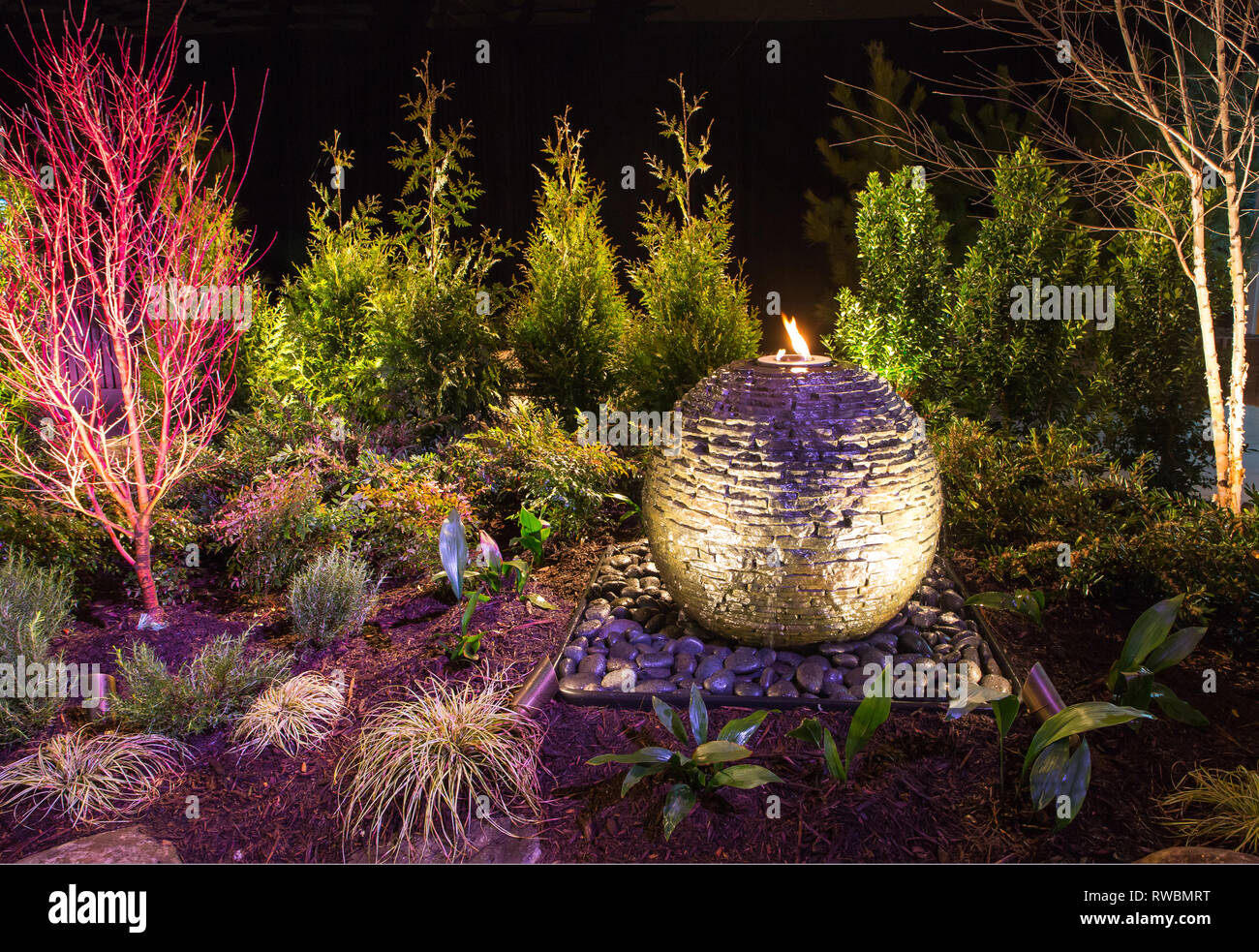 Dramatically lit landscape design with circular stone water fountain. Stock Photo
