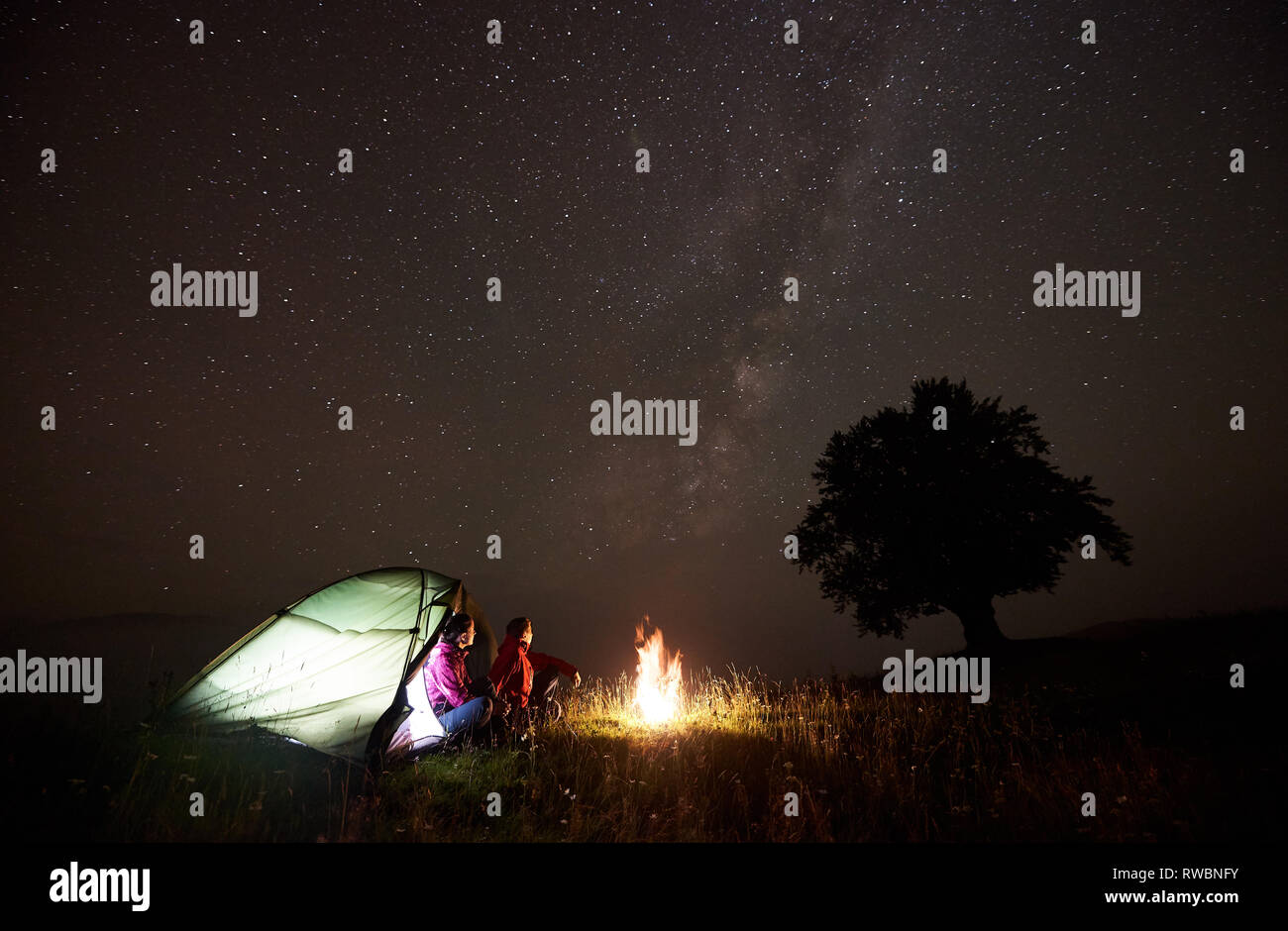 Tourist couple man and woman having a rest near illuminated tent ...