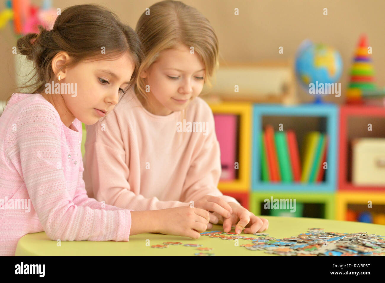 Portrait of cute little girls collecting puzzle pieces while sitting at table Stock Photo