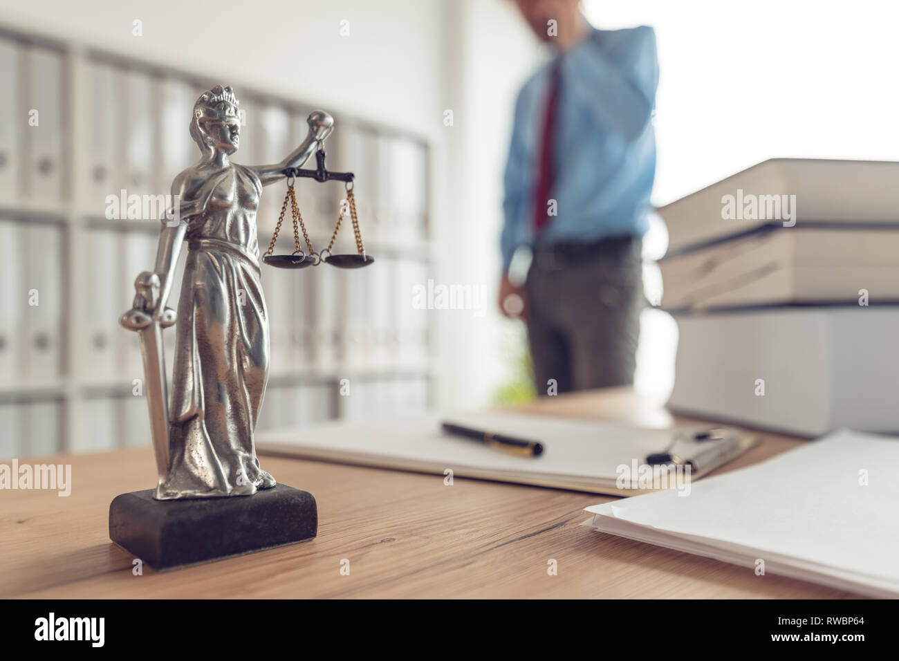 Attorney talking on mobile device in law office, selective focus on statue of Lady Justice Stock Photo
