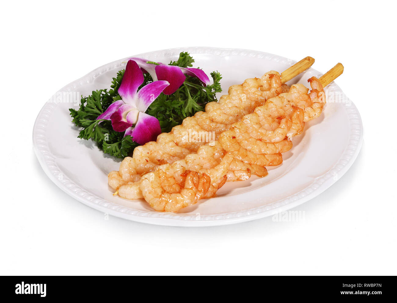 Shrimp skewers according to Chinese tradition. Served on a white plate with salad decoration. Stock Photo