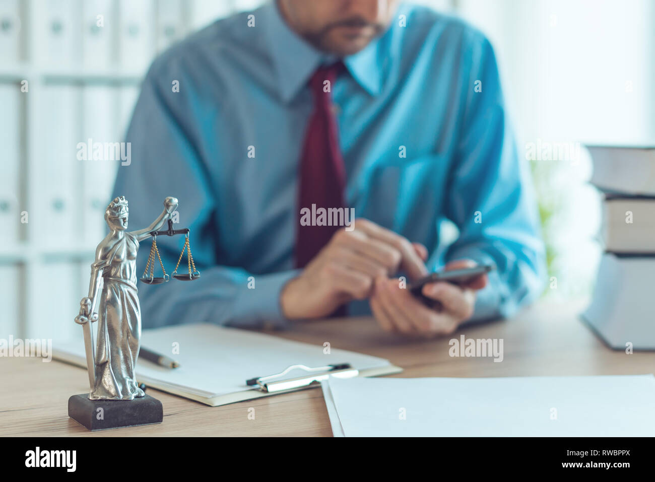 Attorney texting on mobile device in law office, selective focus on statue of Lady Justice Stock Photo
