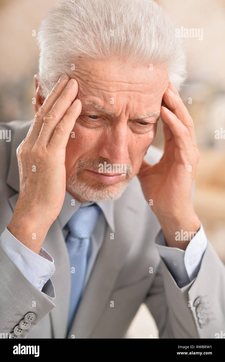 Portrait of senior man with headache holding hands on forehead at home Stock Photo
