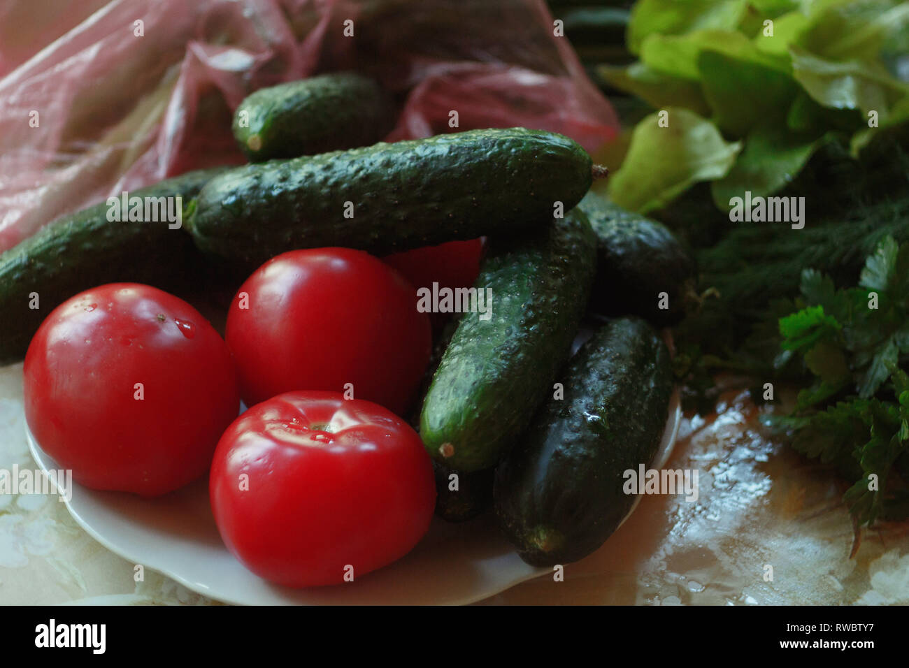 Healthy summer vegetables on the table. Tomatos, cucumbers and greens lying on the table. Stock Photo