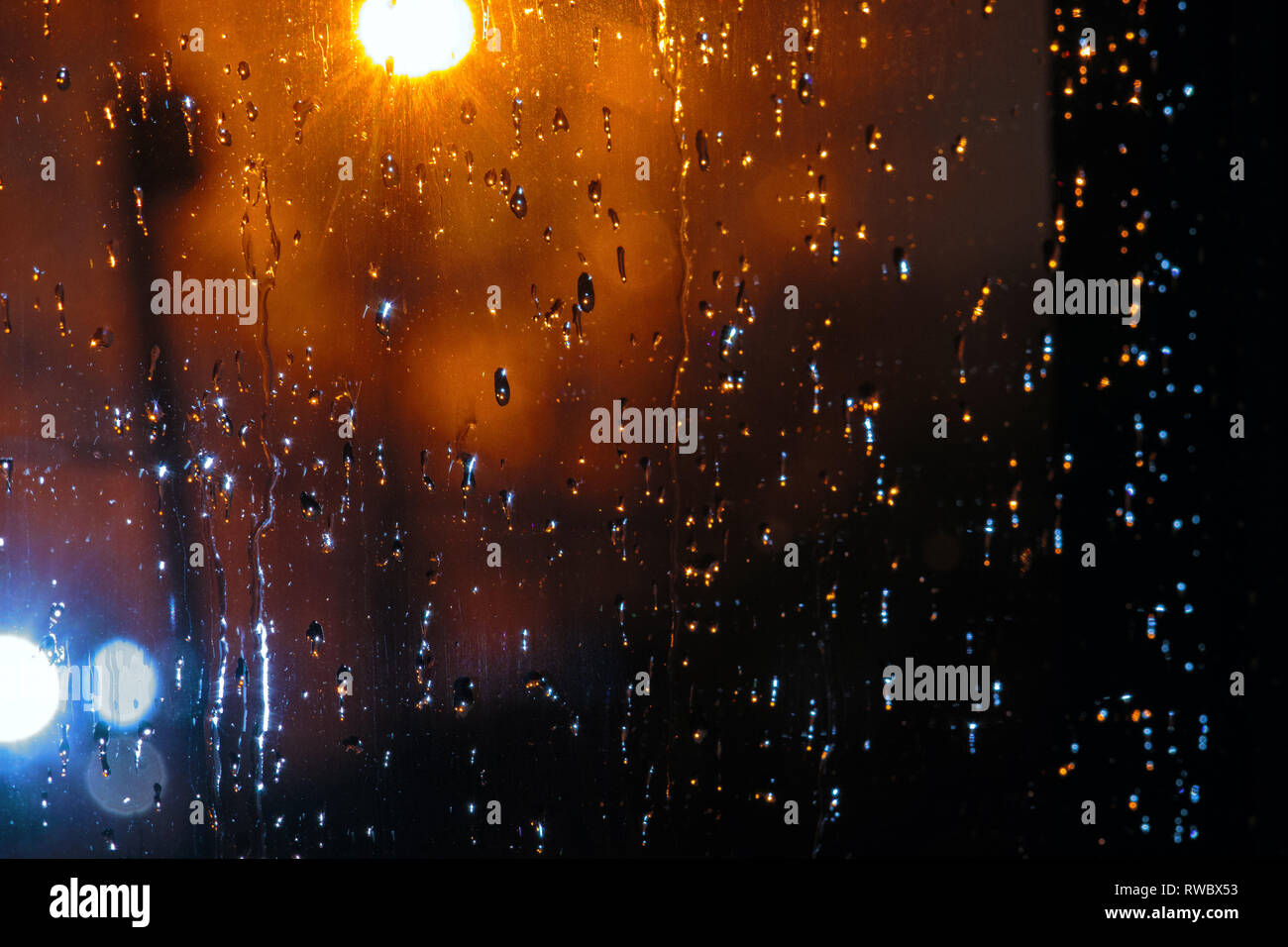 Raindrops on a glass on highlighted background by the flashlight. Water drops on a window glass Stock Photo