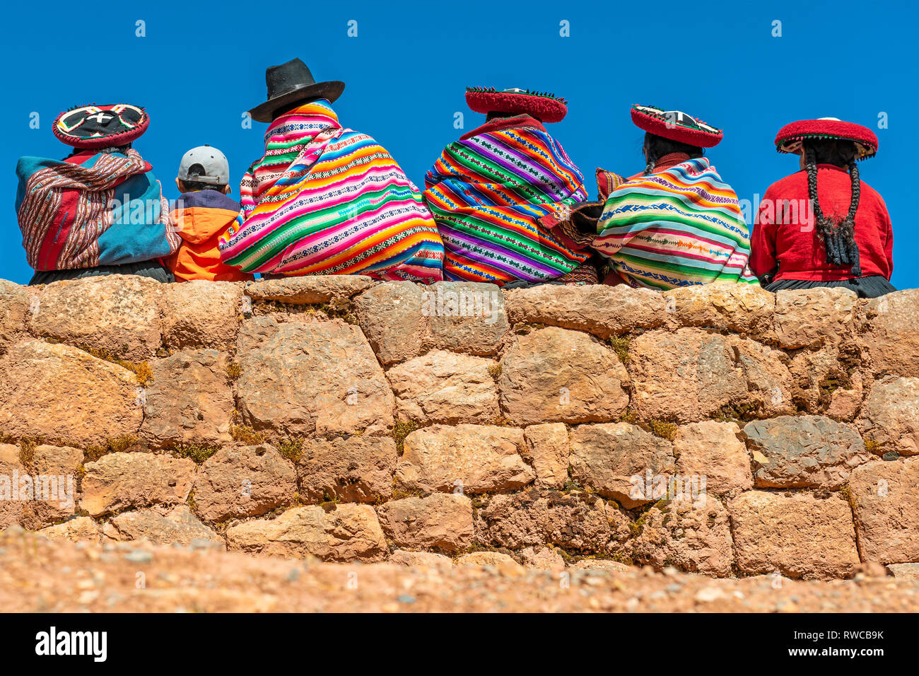 Indigenous Peruvian Quechua women in traditional clothing with a boy sitting on an ancient Inca wall in the ruin of Chinchero, Cusco province, Peru. Stock Photo