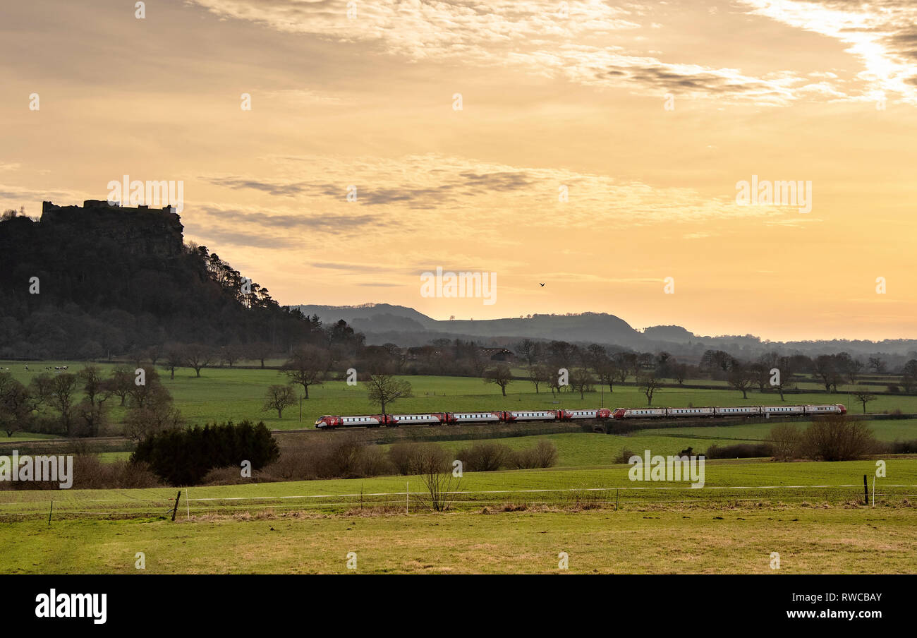 Virgin Voyager train passing Beeston Castle in the golden glow of evening. Stock Photo