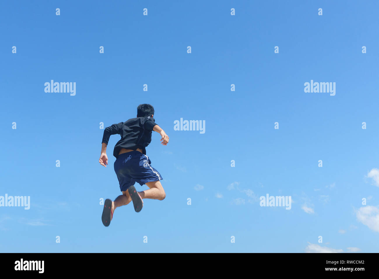 Young man jumping against blue sky landscape. Soft image with the young man is in motion where some blurry effect on his leg to show motion. Stock Photo